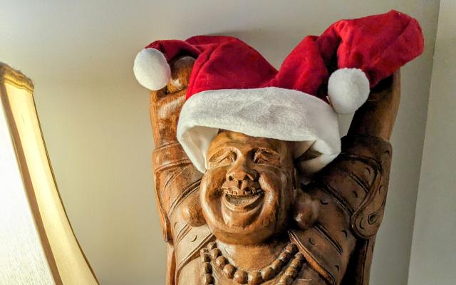 A carved wooden statue of Buddha with a Santa Clause hat placed on Buddha's head