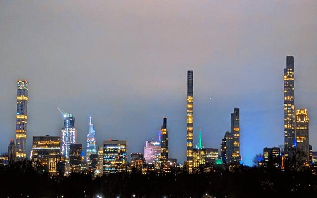 An image of Midtown Manhattan from Central Park with Times Square glowing from its lights