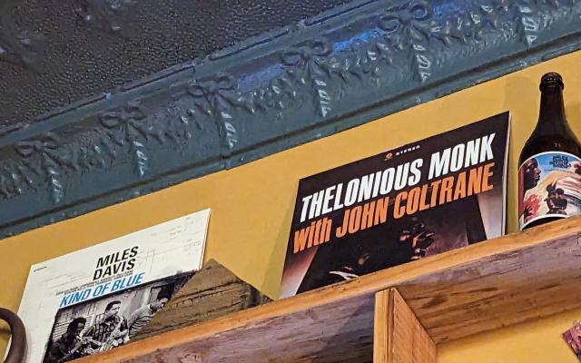 A photo of a high shelf in a bar with a Thelonios Monk with John Coltrane album on it. 